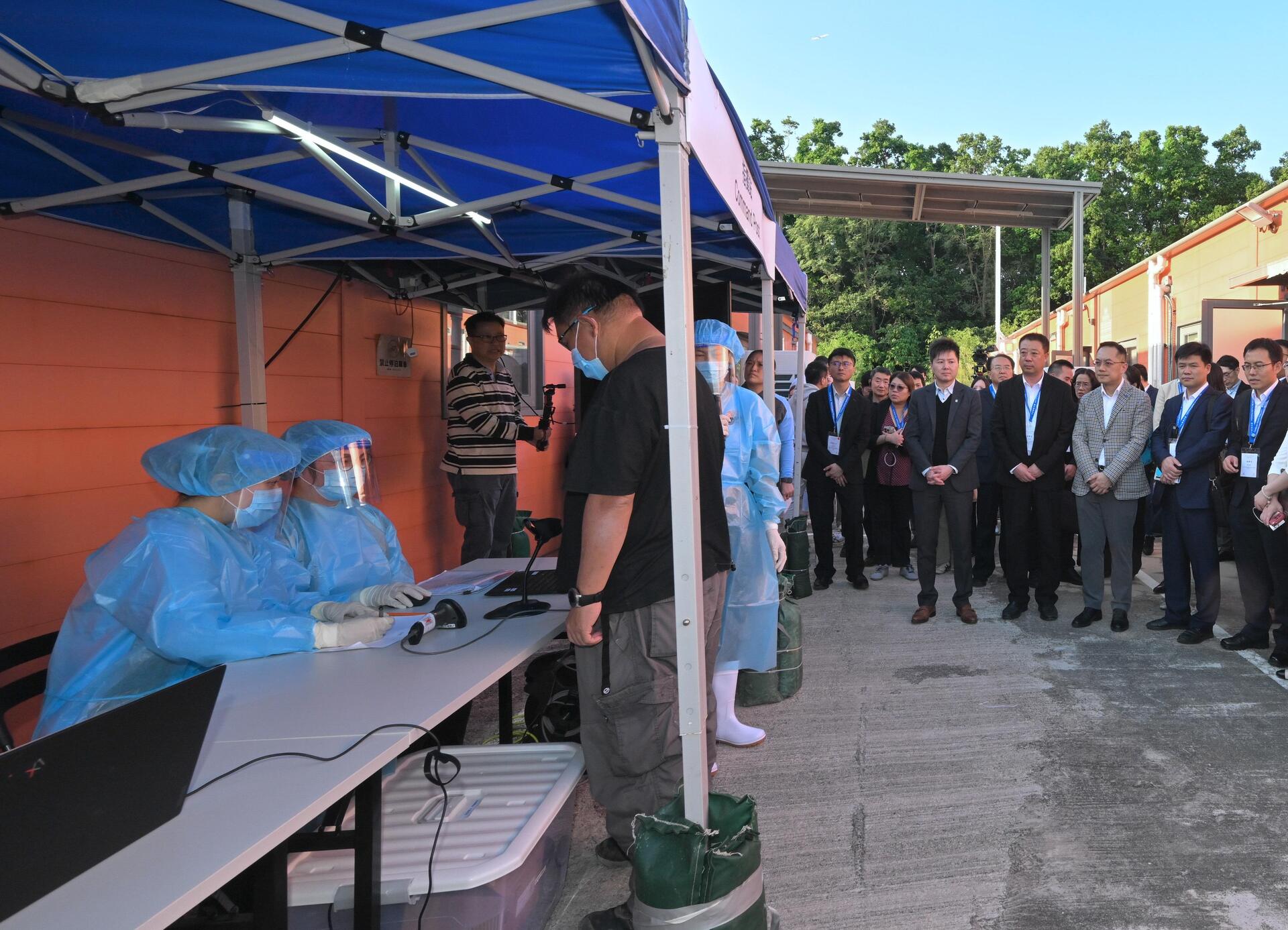 衞生署衞生防護中心今日(十一月二十五日)聯同多個政府部門舉行代號「紫水晶」的公共衞生演習,以提升中心和相關政府部門處理埃博拉(伊波拉)病個案時的應變能力,並提高持份者對處理突發公共衞生事件的意識。為強化與中國內地及國際交流,此次演習亦邀請了來自國家衞生健康委員會、國家疾病預防控制局、陝西省、湖北省、廣東省、粵港澳大灣區內地城市、澳門特別行政區和新加坡衞生當局的20多名專家,以觀察員身分出席。圖示民眾安全服務隊人員為密切接觸者登記入住檢疫設施。衞生署署長林文健醫生(右三)和多位觀察員在旁視察。