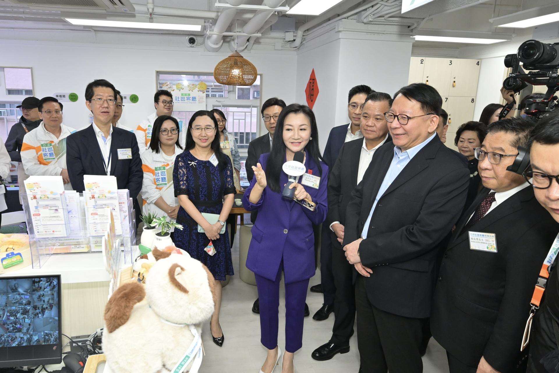 香港岛妇女联会主席金玲(中)向政务司司长陈国基介绍西环社区客厅内“特色职员”AI猫。