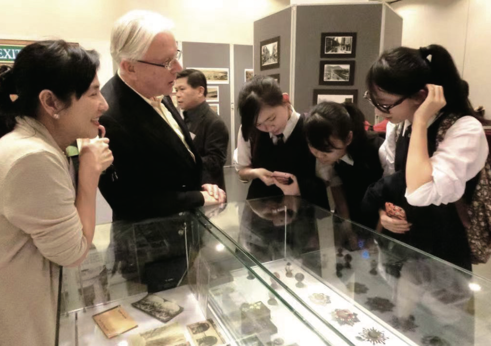 江乐士40余年长居香港,发展了一项爱好——中国历史,并嗜好收藏古物。图为2013年,他在香港中央图书馆展出收藏时,向中学生讲解。身旁是夫人Elaine 截屏2022-03-01 上午9.53.30