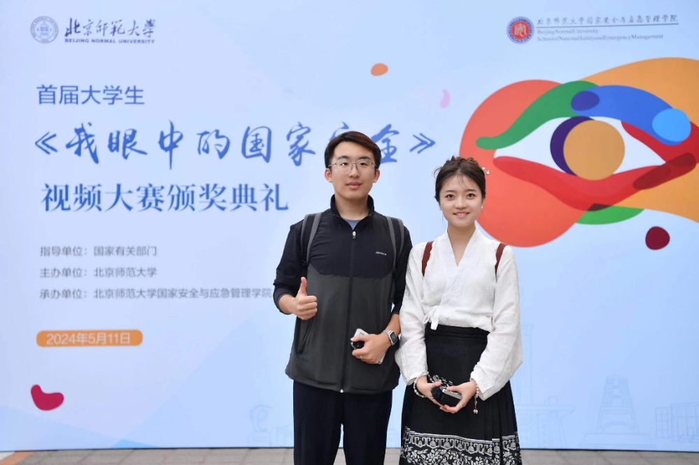 A person and person standing in front of a large sign
Description automatically generated